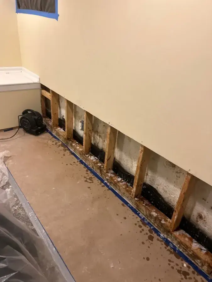 Drywall cut out in a strip along the bottom of a wall with plastic sheeting on the floor