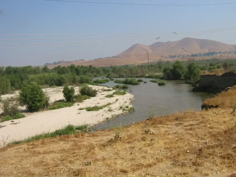 Shallow river winding through a sandy channel below dry brown hills