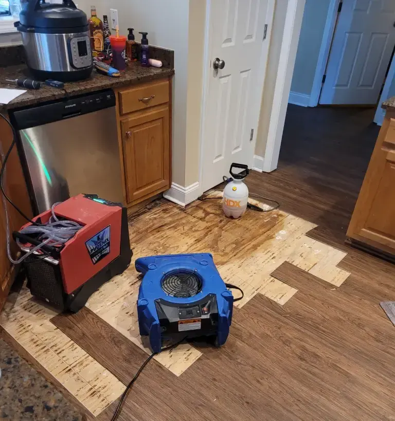 Kitchen with the flooring cut back in front of a dishwasher and drying equipment running