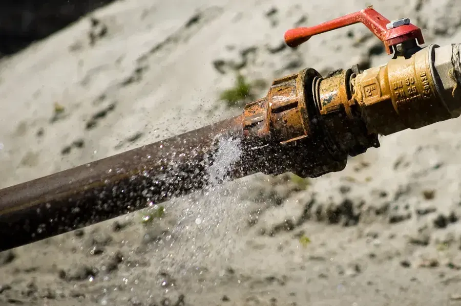 Water spraying out of a split pipe beside a brass shutoff valve