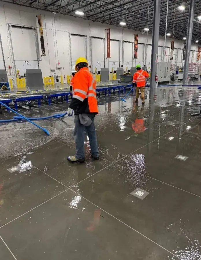 Workers in high-visibility vests clearing water from a large warehouse floor