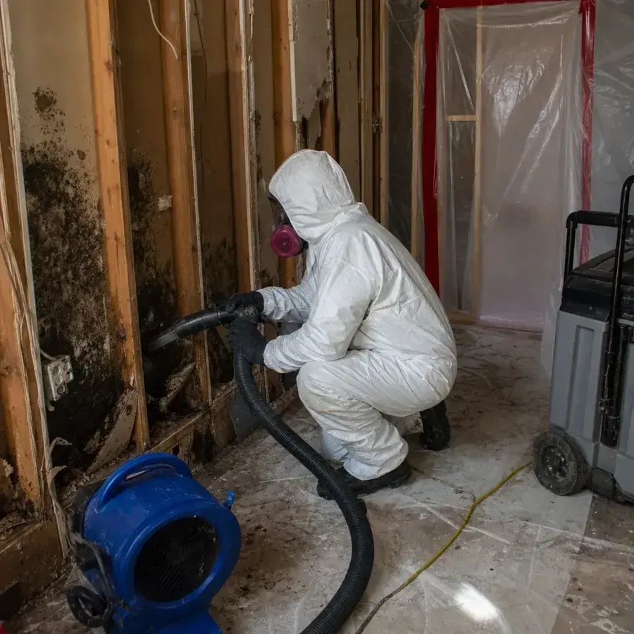 Technician in a protective suit and respirator extracting a gutted room behind containment