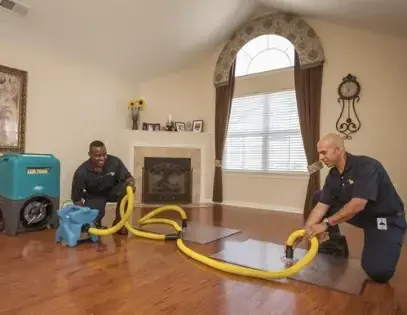 Two technicians laying drying mats and hoses on a wood floor next to a dehumidifier